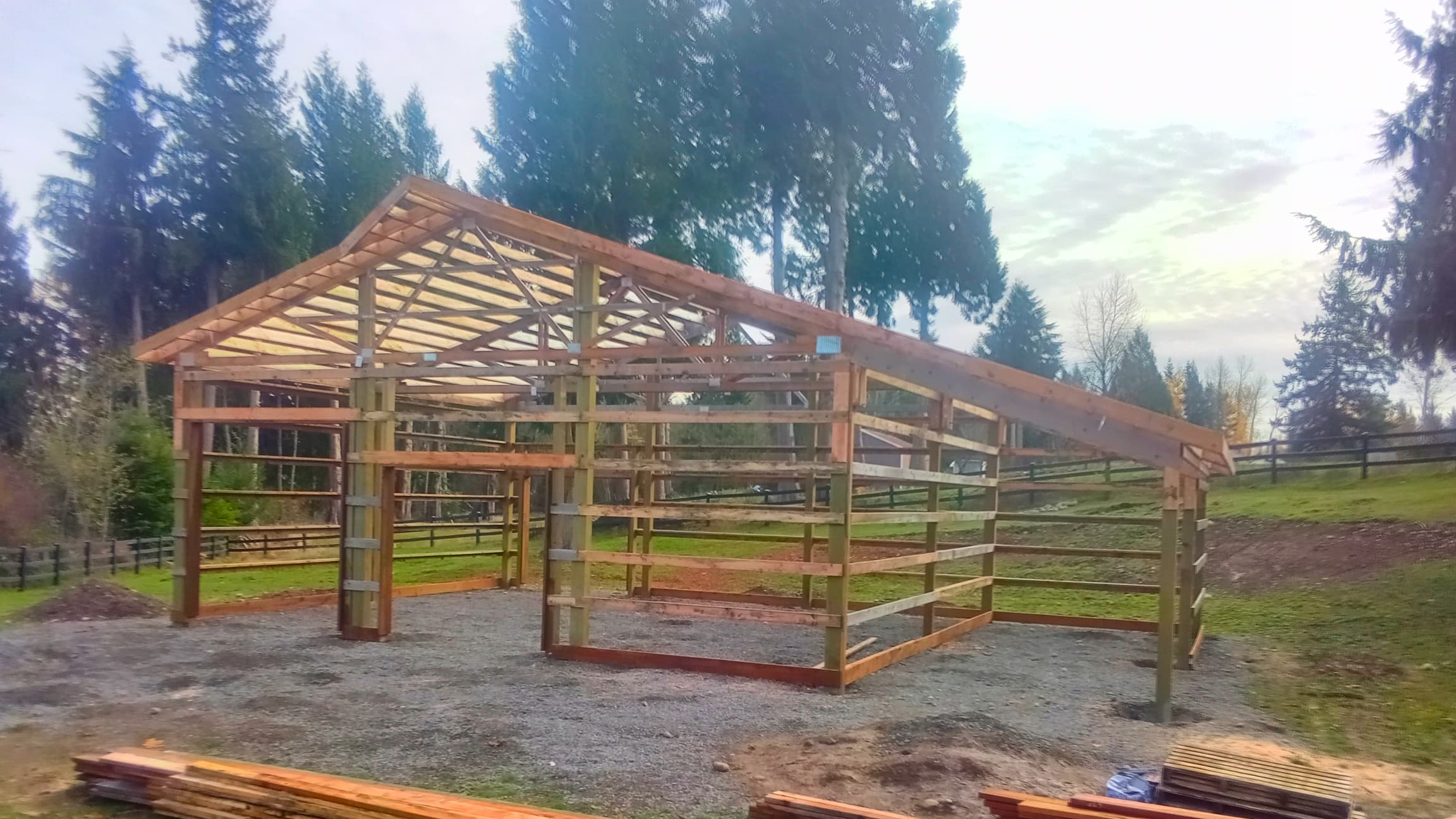 Progress photo of a 36'x36' post-frame building with roof trusses installed on a prepared gravel foundation. This Probuilt Metal Buildings structure in Lake Tapps shows the sturdy wood framework that will support metal siding and roofing, creating a versatile shelter for vehicles, equipment, or workshop space.